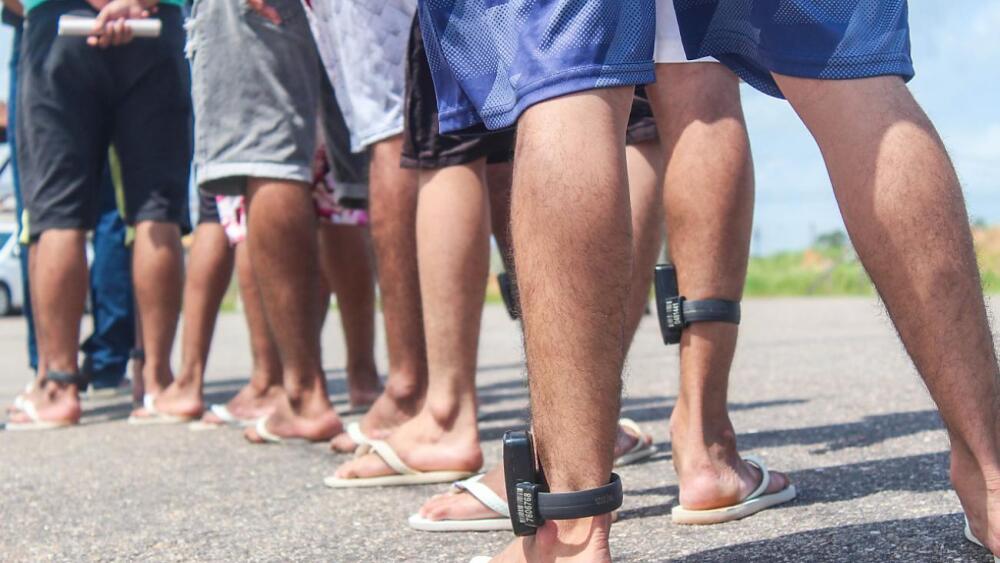 Presos com tornozeleira eletrônica formam fila em presídio; seus rostos não aparecem na foto