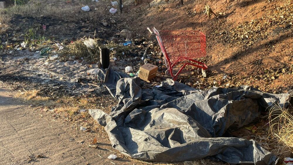 Corpo coberto por lona preta ao lado de carrinho de supermercado