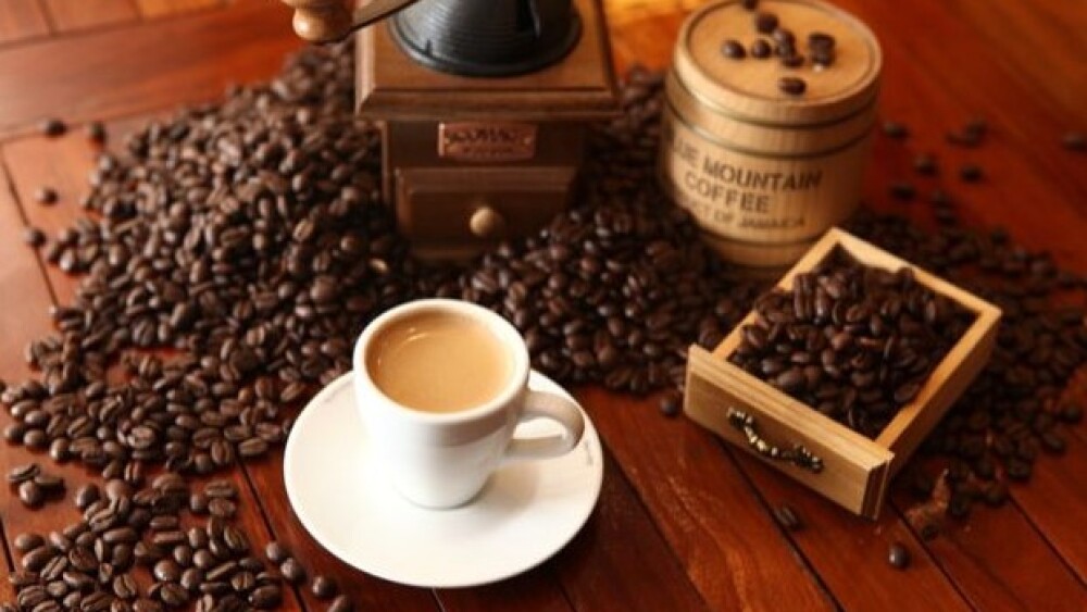 Mesa de madeira com grãos de café e uma xícara com o café feito