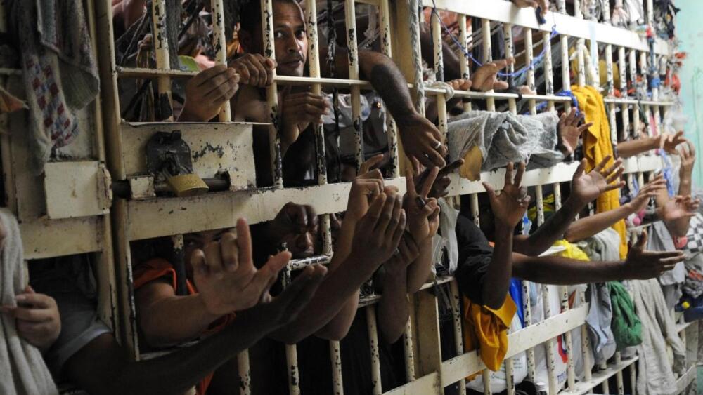 imagem mostra braços de presos para fora das grades em presídio